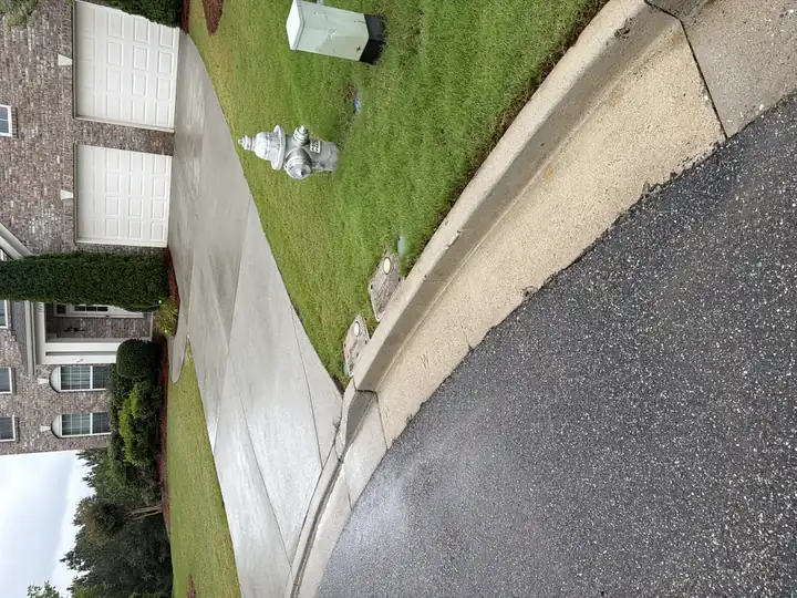 Pressure-washed concrete driveway and curb apron after cleaning in Cumming, GA, wide street view with brick home
