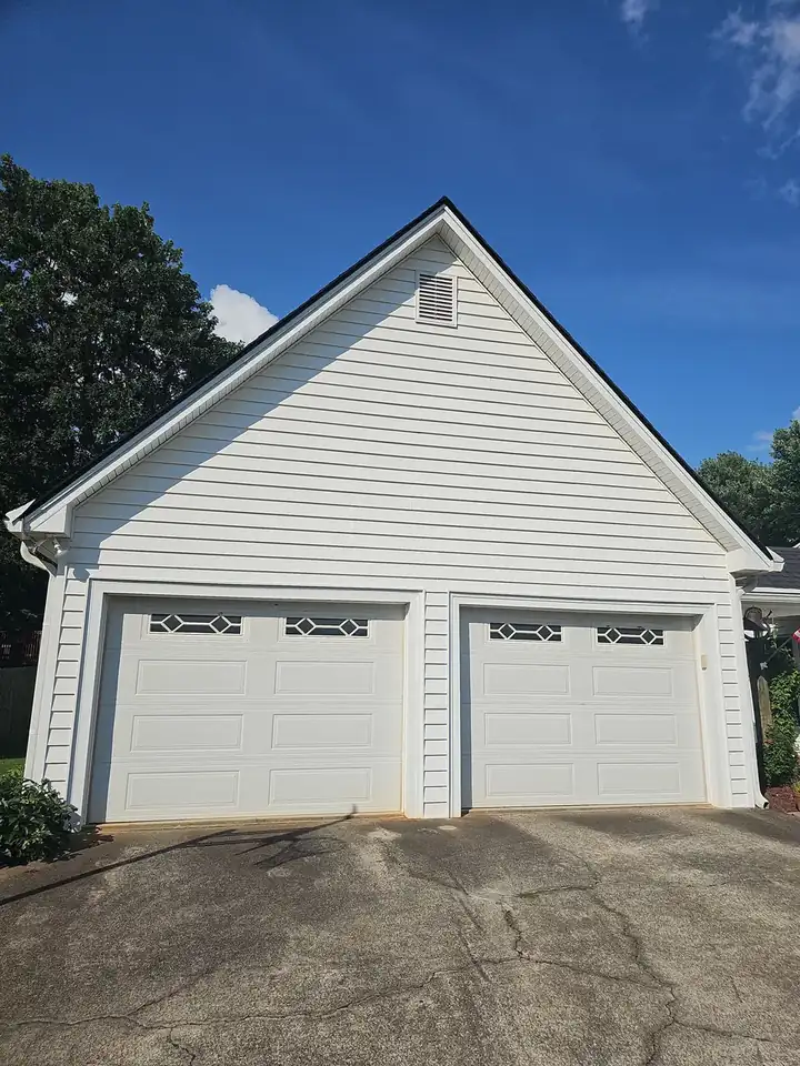 Two-car detached garage with white vinyl siding and white garage doors under a clear blue sky after a house wash in Kennesaw, GA.