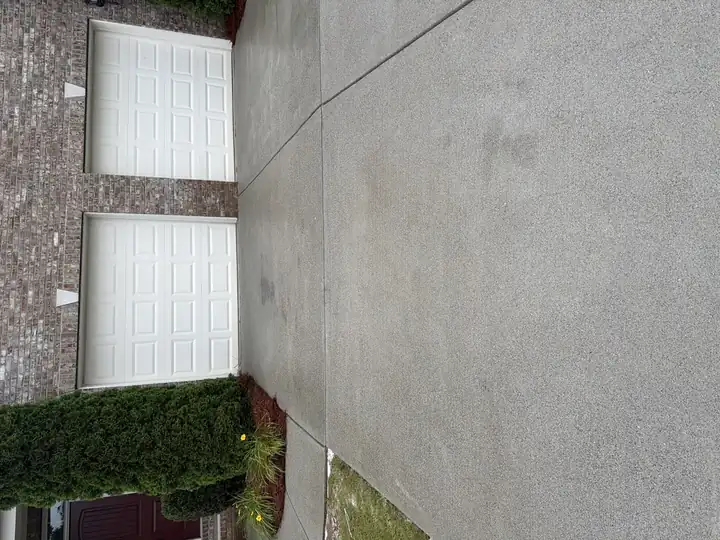 Pressure-washed two-car concrete driveway in Cumming, GA with brick home and cedar bushes, surface looking clean and uniform