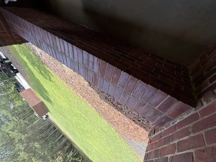 Clean brick patio wall and landscaping edge after pressure washing in Alpharetta, GA, with bright mortar joints and green lawn visible beyond the wall