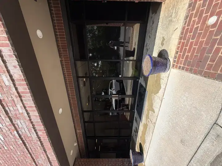 Commercial building front entrance and concrete apron during pressure washing in Alpharetta, GA, with wet pavement, glass storefront, and potted planters visible