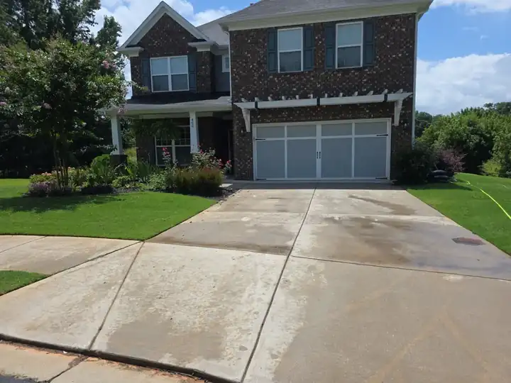 Wide-angle view of a concrete driveway at a two-story brick home in Canton, GA, with staining and discoloration visible on the surface.