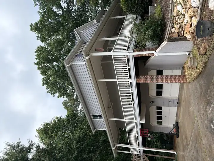 Full front view of two-story Canton, GA home with clean gray vinyl siding, wrap-around porch, and brick garage after house wash