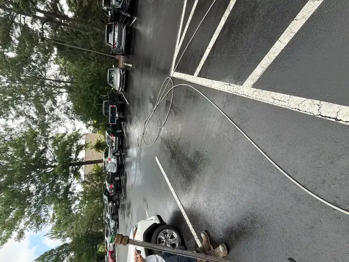 Asphalt commercial parking lot being cleaned in Alpharetta, GA, with pressure hose coiled on wet pavement and vehicles still parked along the perimeter