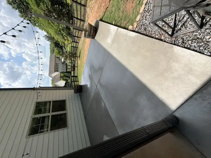 Wet freshly pressure-washed concrete covered patio in Canton, GA, string lights overhead, barrel planter and gravel border visible