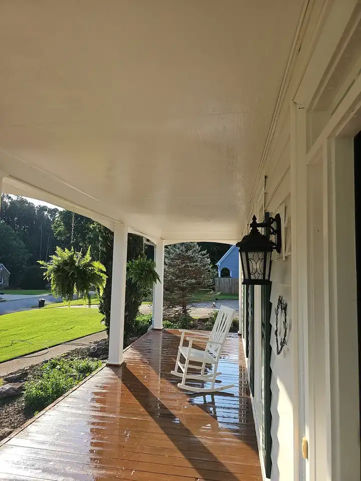 Covered front porch deck still wet from washing, white columns and a rocking chair visible, during a house wash in Kennesaw, GA.