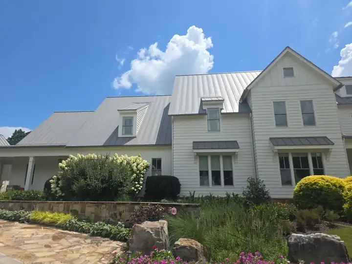 Wide view of white vinyl siding and standing-seam metal roof on a two-story farmhouse in Milton, GA.