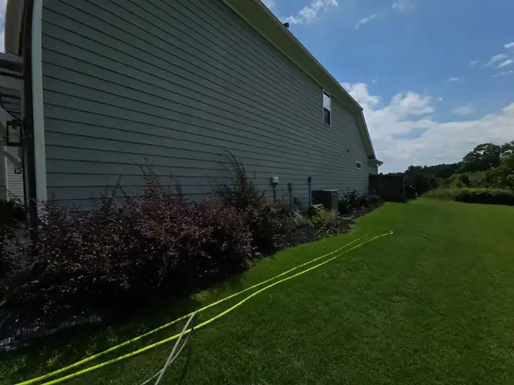 Side of a gray vinyl-sided home with garden beds and pressure washing hose on the lawn in Canton, GA.