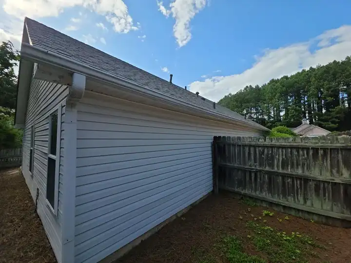 Rear corner of a residential home showing vinyl siding, gutters, and a wood privacy fence in Woodstock, GA.