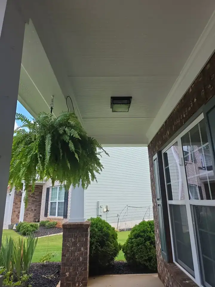 Front porch beadboard ceiling with hanging fern basket and brick columns at a house washing job in Canton, GA.