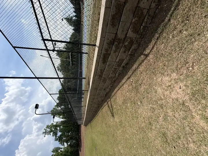 Stone retaining wall and black chain-link pool fence before pressure washing at a commercial property in Canton, GA, showing algae and dirt buildup