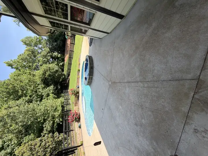 Dirty concrete pool deck in Canton, GA, with bright blue pool water and lush tree backdrop.