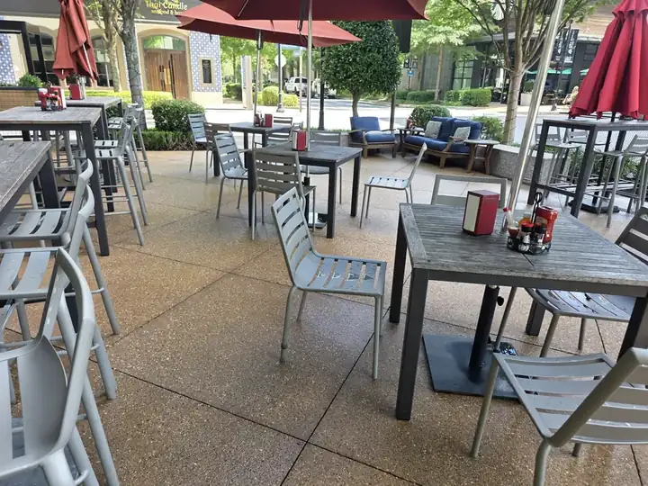 Exposed-aggregate concrete patio with dining tables and red umbrellas at a commercial pressure washing job in Alpharetta, GA.