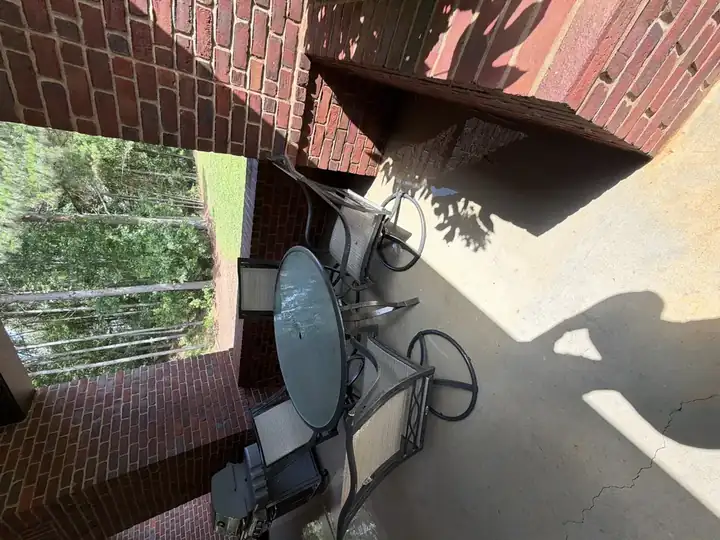 Clean covered concrete patio after pressure washing in Alpharetta, GA, with outdoor dining set, brick columns, and a gas grill visible in natural light