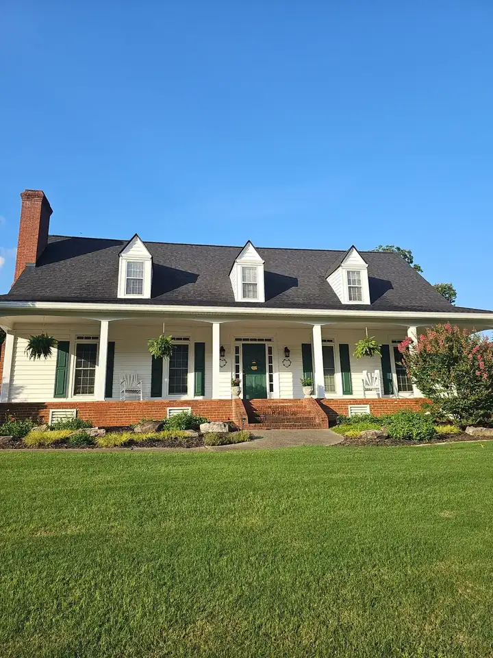 Full front view of a large white house with a wraparound covered porch, green shutters, and a brick foundation after a house wash in Kennesaw, GA.