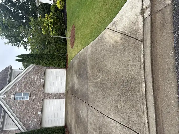 Concrete driveway with algae and grime buildup before pressure washing in Cumming, GA, brick home with two-car garage