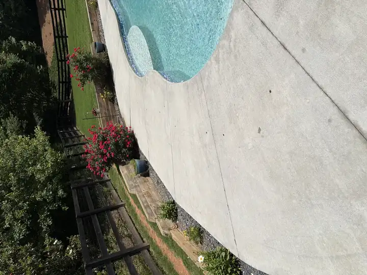 Clean concrete pool surround after pressure washing in Canton, GA, with rose bushes and black split-rail fence in the background