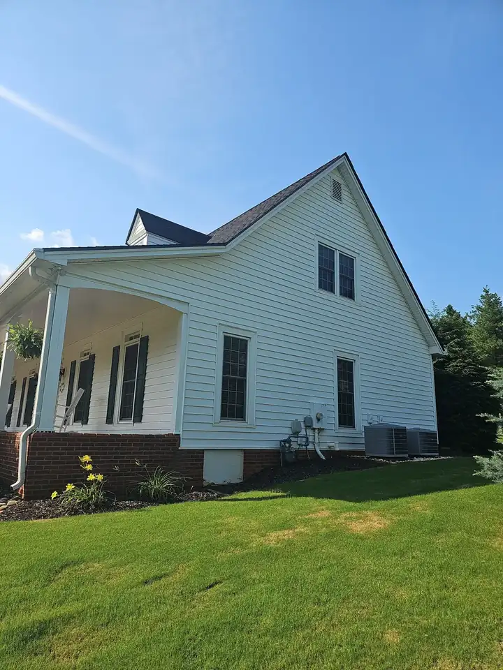 Side view of a white two-story home with vinyl siding, black shutters, and a covered porch corner after a house wash in Kennesaw, GA.