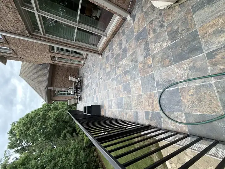 Wide view of a tile-paved upper deck with iron railing and garden hose coiled in the foreground at a Duluth, GA home.