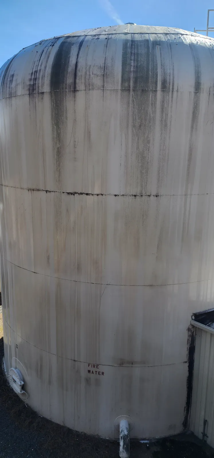Tall industrial storage tank covered in dark stains before pressure washing, with a ladder and the number 8 on the shell.