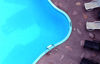 a pool seen fram above with a concrete pation and patio chairs